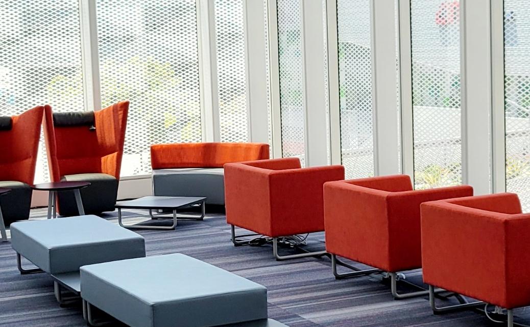 grey & orange lounge furniture in a sunlit space with grey carpet and high windows